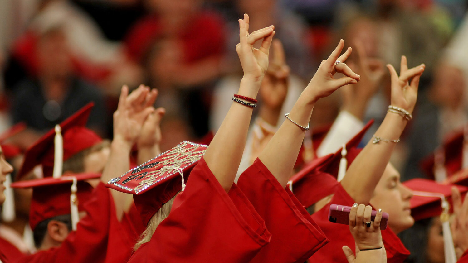Wearing caps and gowns, students hold up the "Wolfie" sign