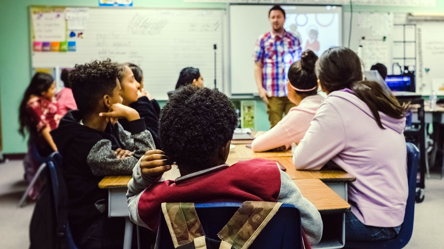 A multicultural mix of middle school students listen to a teacher in a classroom.