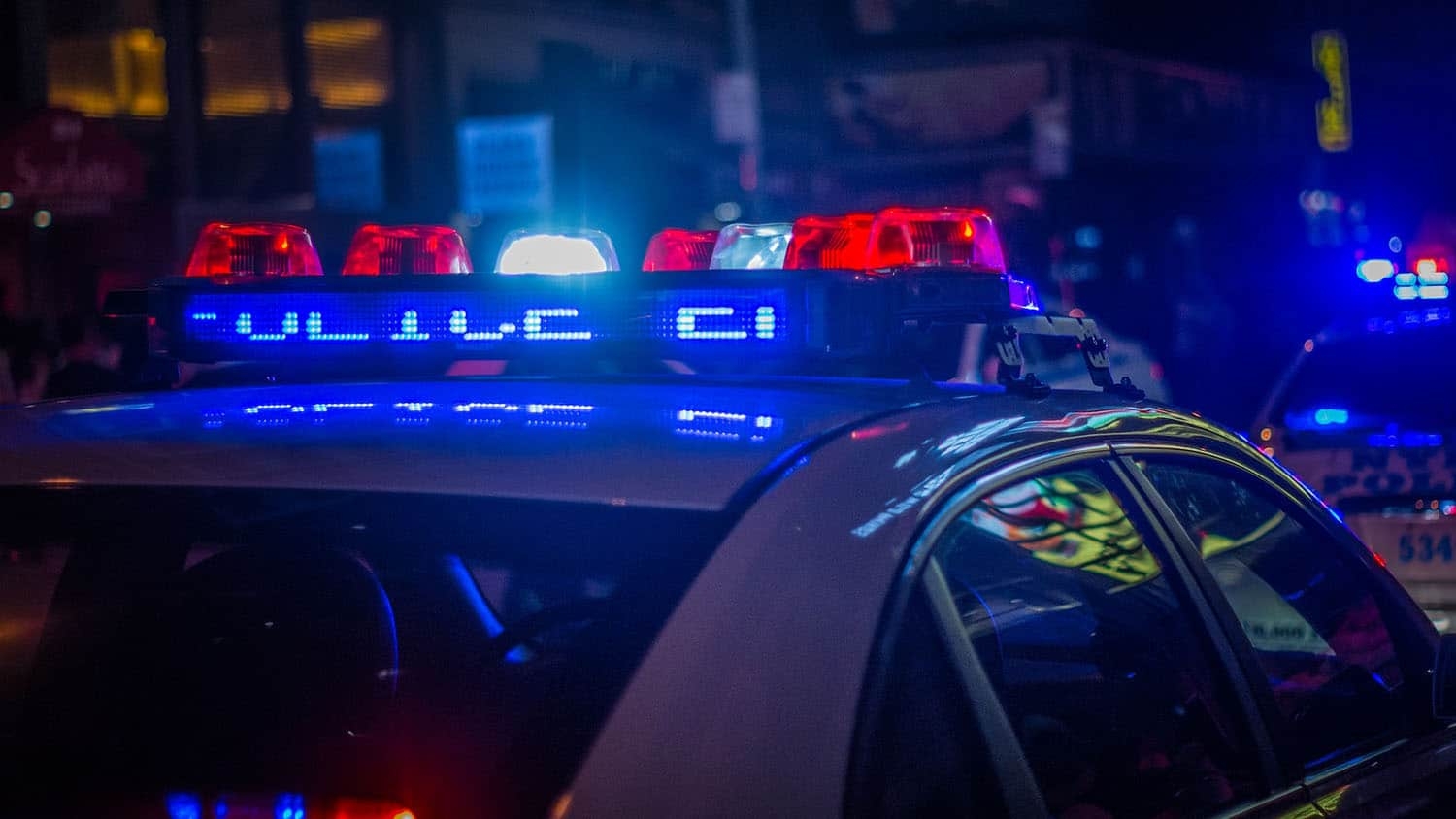photo shows red and blue lights flashing atop a police car at night